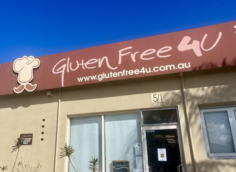 Looking up at a sign above a glass door that says "Gluten Free 4U"