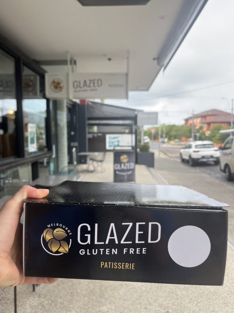 A hand holding a black takeaway box that says "Glazed Gluten Free