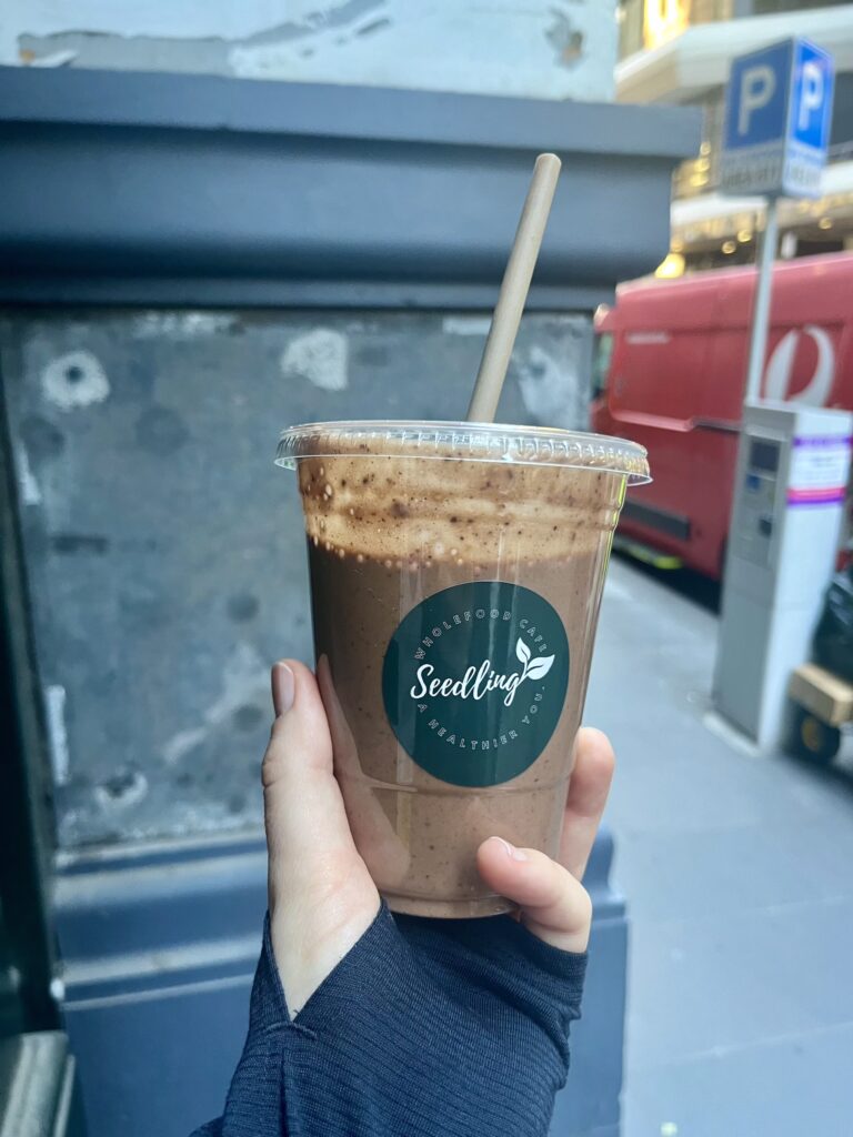 A hand holding a chocolate coloured smoothie with a straw